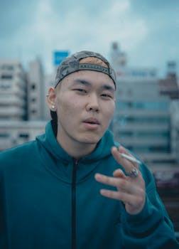 Young adult smoking outdoors in Shinjuku, Tokyo. Urban casual style with cap and hoodie.