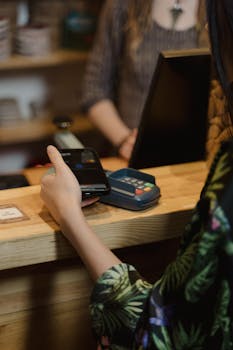 A person using mobile to make a contactless payment at a café counter.