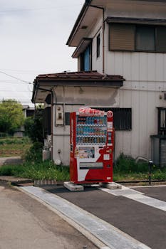 A red vending machine stands outside a traditional Japanese house, capturing everyday Japan.